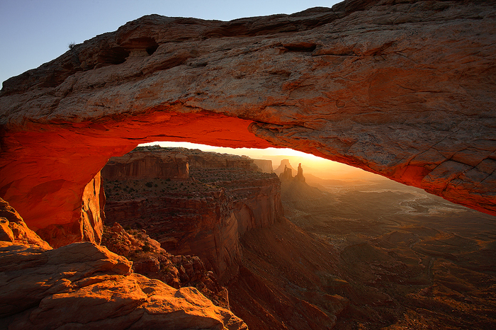 The sun rises over the La Sal mountains awakening Canyonlands and Mesa Arch with a beautiful warm orange glow.